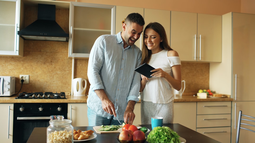 Attractive couple meet in the kitchen early morning. Handsome woman using tablet sharing his husband social media at home