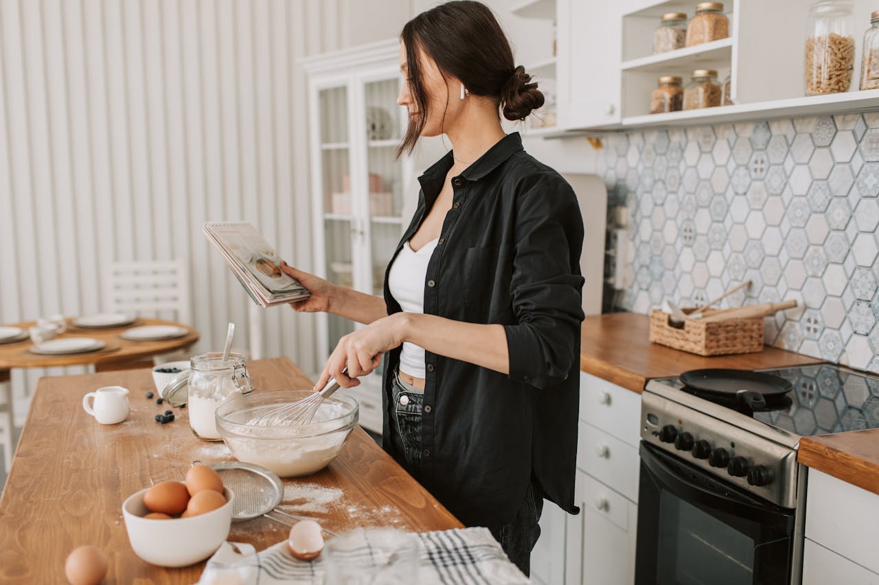 Woman in kitchen holding a cookbook and mixing ingredients for a recipe.